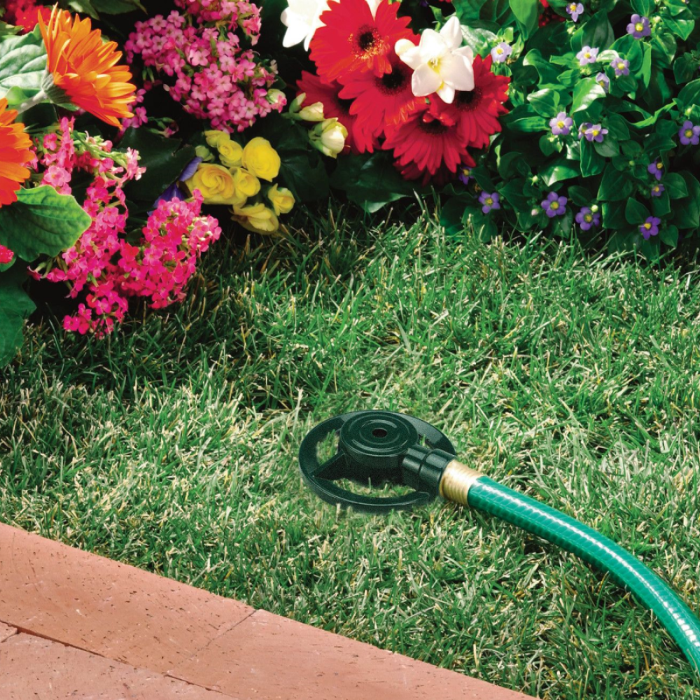 Dad's reliable zinc spot sprinkler connected to a garden hose, lying on grass and surrounded by beautiful flowers.