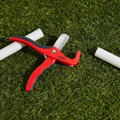 A red tubing cutter laying on the grass. 